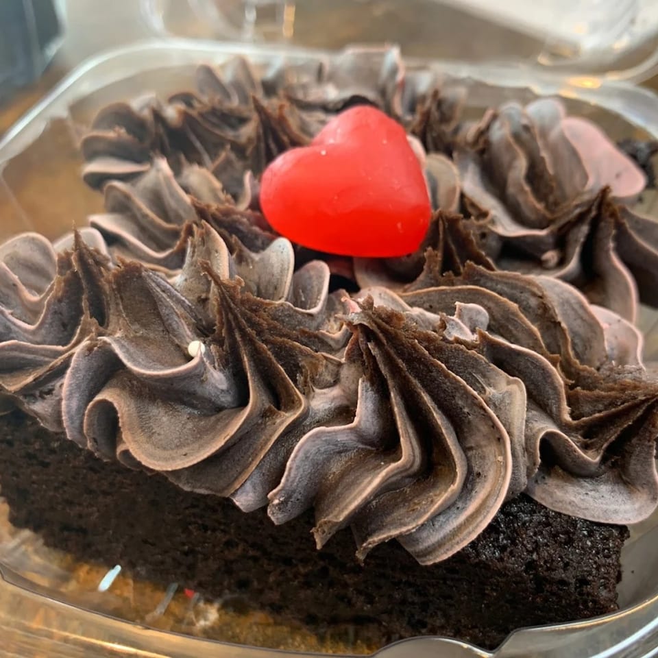 A chocolate cupcake with dark chocolate frosting and a red heart candy on top.