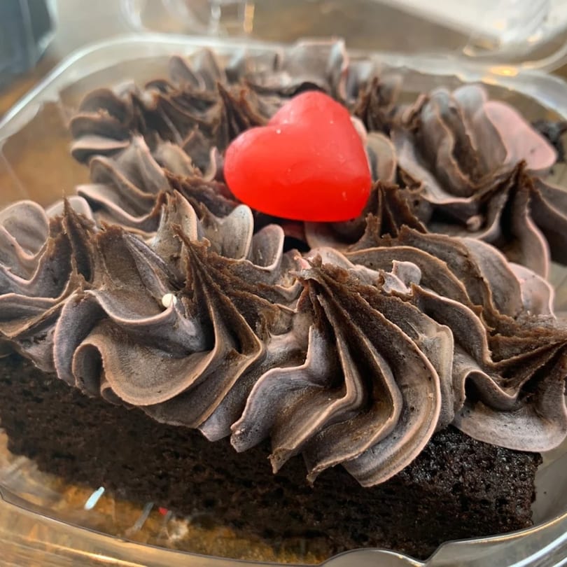 A chocolate cupcake with dark chocolate frosting and a red heart candy on top.