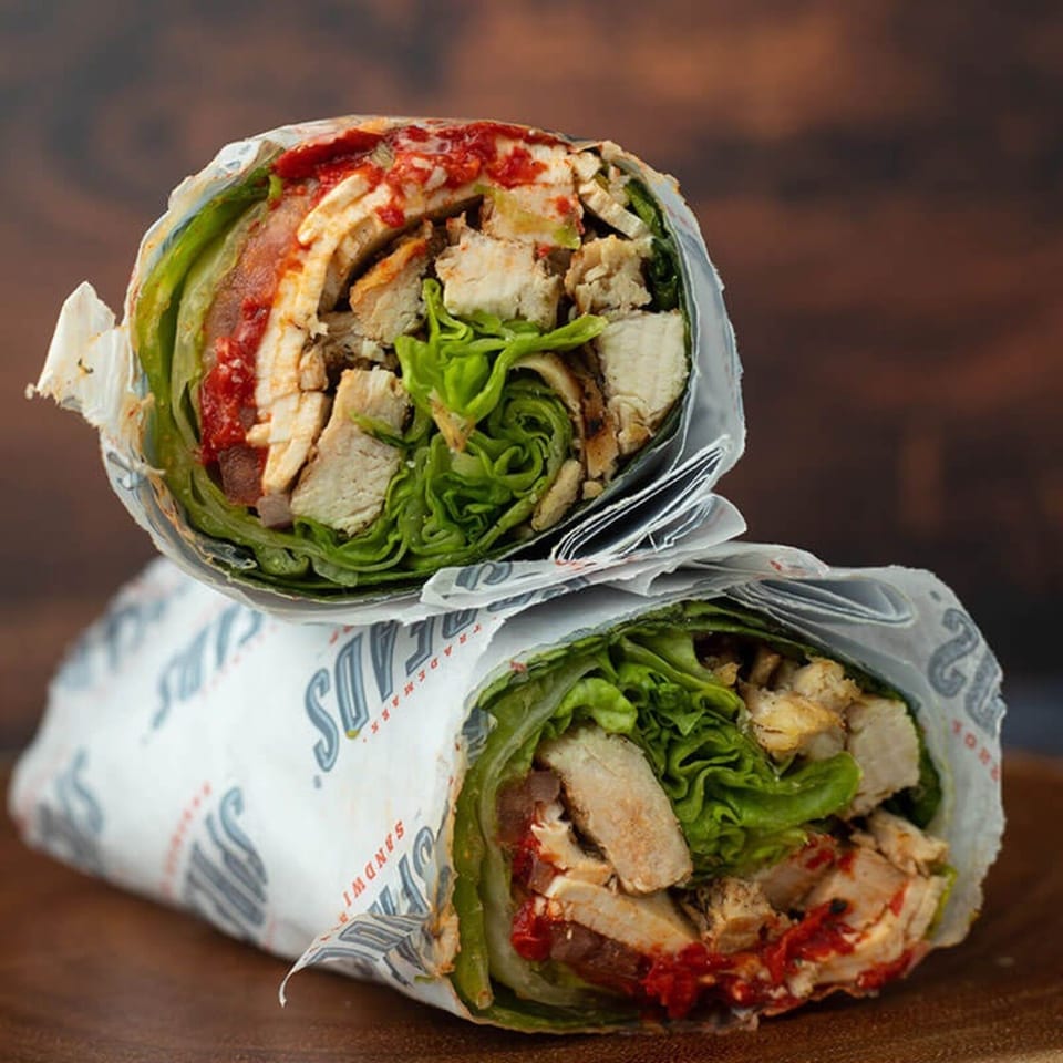 Two chicken wraps, filled with lettuce and red sauce, stacked on a wooden surface.