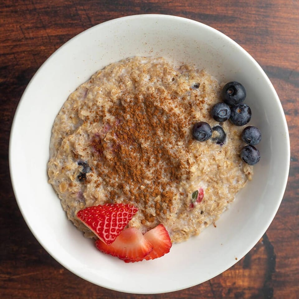 Oatmeal with cinnamon, blueberries, and sliced strawberries in a white bowl on a wooden table.