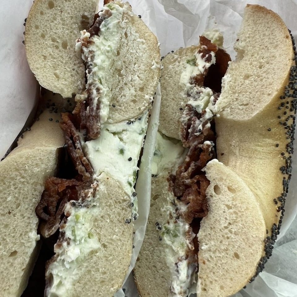A poppy seed bagel from Bagel & Deli Creations, sliced in half with cream cheese and bacon.