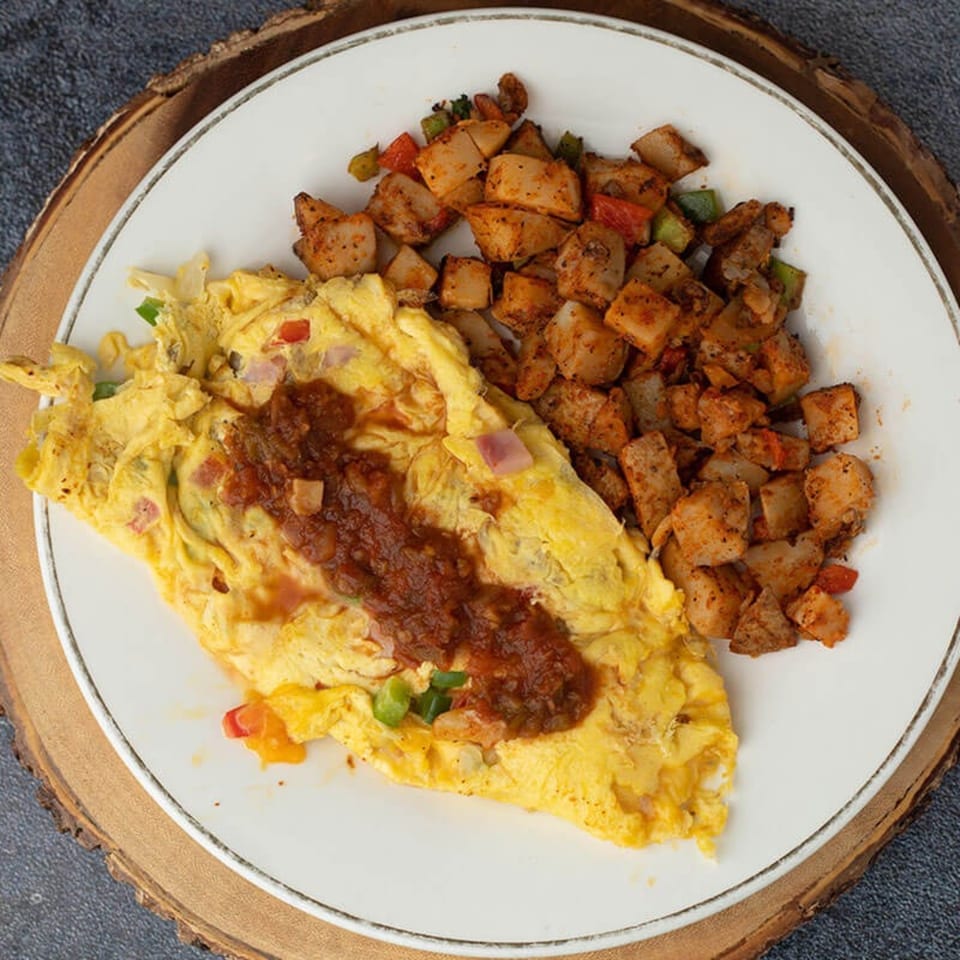 Omelet topped with salsa and a side of seasoned breakfast potatoes on a white plate.